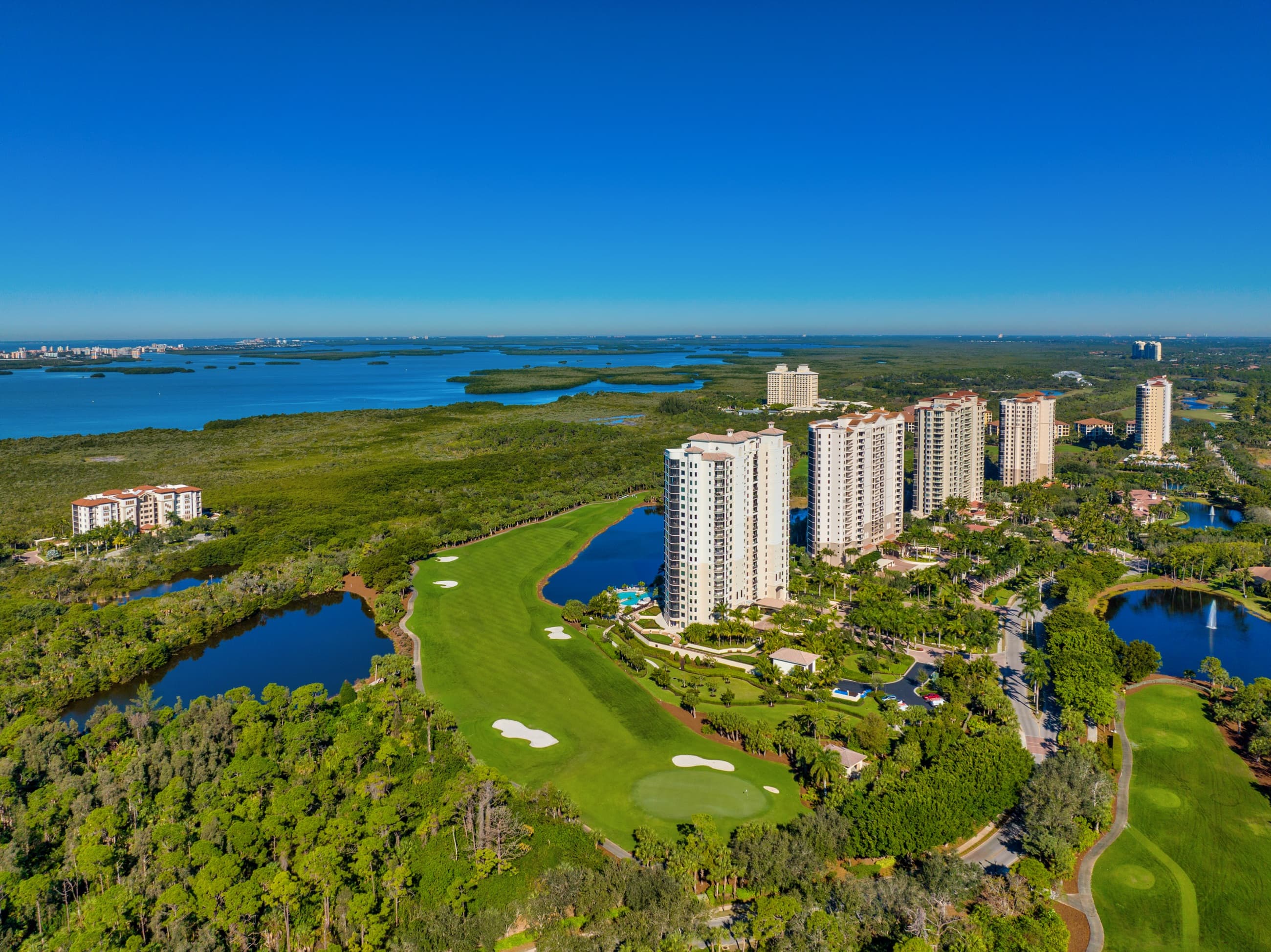 Aerial view of The Colony at Pelican Landing — high-rise towers and championship golf above Estero Bay in Bonita Springs, Florida